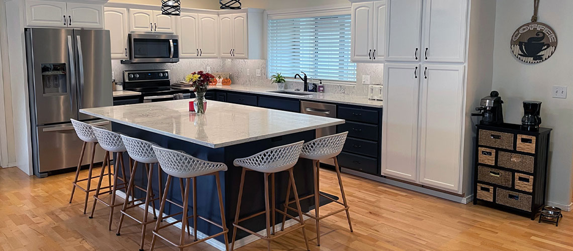A kitchen with navy blue base cabinets, white quartz countertops, and oak flooring.
